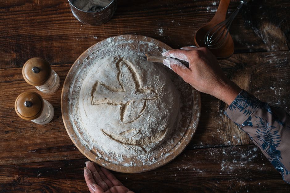 Baker shaping a round of dough on a floured wooden bench